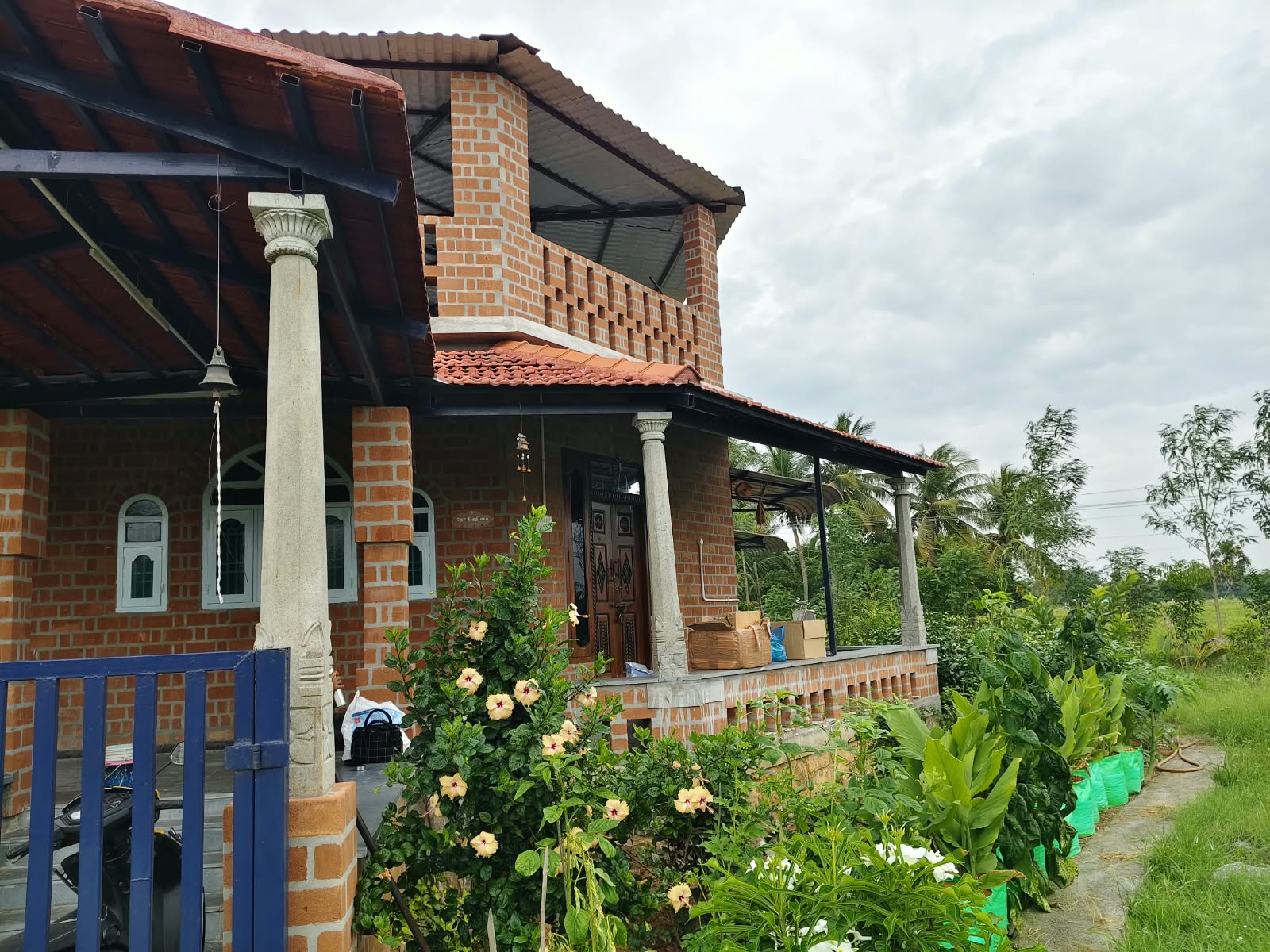 Joe's Nithilam farmhouse veranda with carved stone pillars and hibiscus garden